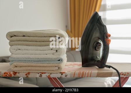 A pile of towels and an iron on the ironing board. Homework concept. Stock Photo
