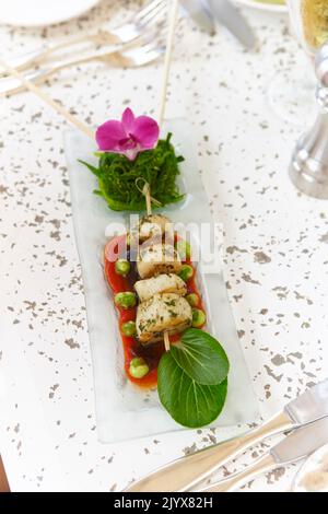 Gourmet cooked scallop dish with seaweed salad and baby bok choi park choi leaves.  Served on a long rectangular glass plate for special occasion. Stock Photo