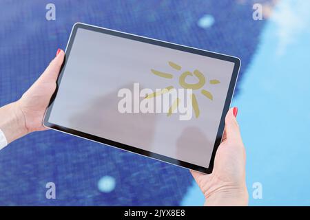Female hands hold tablet with drawn sun and white screen above pool Stock Photo