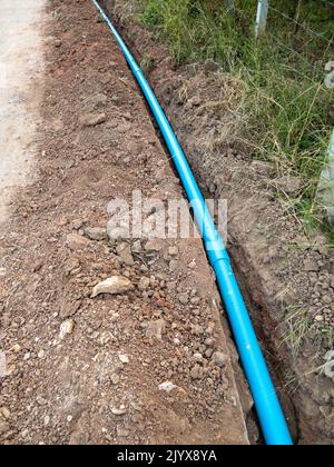 The new PVC pipe is laying in the trench along the concrete road for the water supply system of the rural village, front view with the copy space. Stock Photo