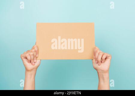 Woman hands holding blank rectangular sheet of brown cardboard on light blue background Stock Photo