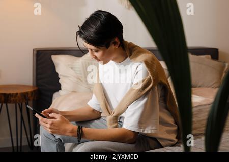 Asian boy using mobile phone while sitting on bed at home Stock Photo