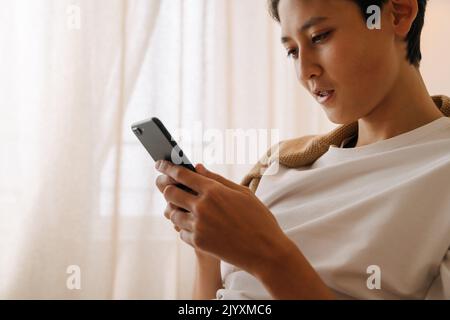 Asian boy with brace using mobile phone while resting at home Stock Photo