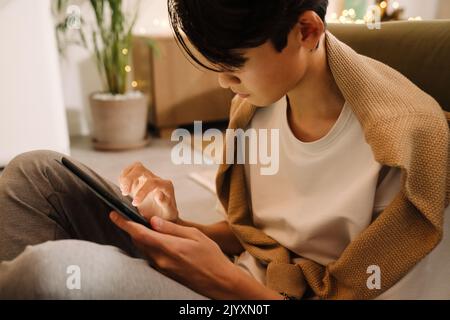 Asian boy using tablet computer while sitting on floor at home Stock Photo