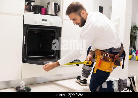 Young Male Technician Repairing Oven In Kitchen Stock Photo