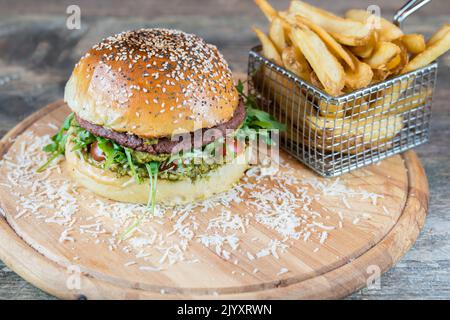 Vegan hamburger with no meat alternative. Plant based burger with pesto, vegan cheese and fried potatoes. Healthy street and fast food. Homemade bun. Stock Photo