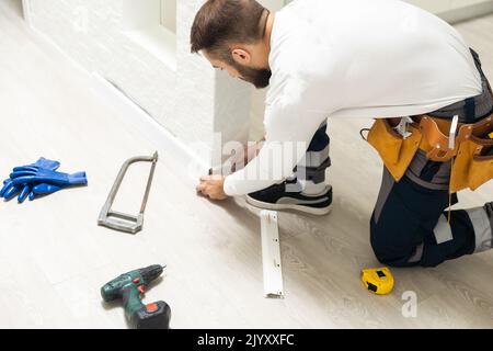 The craftsman measures the length of the plinth for cutting, installing the plinth on the corner of the wall, close-up installation Stock Photo