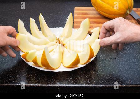 People take sliced ripe juicy melon slices from the plate with their hands. Delicious healthy food. Stock Photo