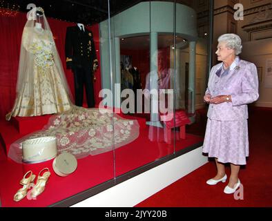 File photo dated 24/7/2007 of Queen Elizabeth II looking at her 1947 wedding gown and 13-foot bridal trail designed by Norman Hartnell, andthe naval uniform worn by the Duke of Edinburgh, which are on show for the Summer Opening Exhibition at Buckingham Palace to mark her Diamond Wedding Anniversary. The Royal couple were the country???s Prince Charming and Fairy Princess and their wedding in Westminster Abbey captured the public imagination in the austere post-war days as the first great state occasion in the post-war years and a distraction from the hardships the Second World War had imposed Stock Photo