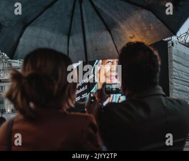 Tourists capture an image of Queen Elizabeth II displayed on the screen at Piccadilly Circus shortly after her death was announced. Stock Photo