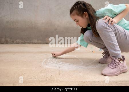 Girl draws with colorful crayons on pavement. Children's drawings with chalk on wall. Creative kid. Joy of childhood. High quality photo Stock Photo