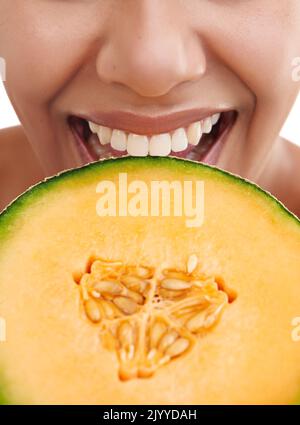 Delicious and good for you. Cropped studio shot of a young woman biting into a piece of melon. Stock Photo