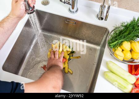 A hand shoves food waste into a disposer hole in the kitchen sink Stock Photo