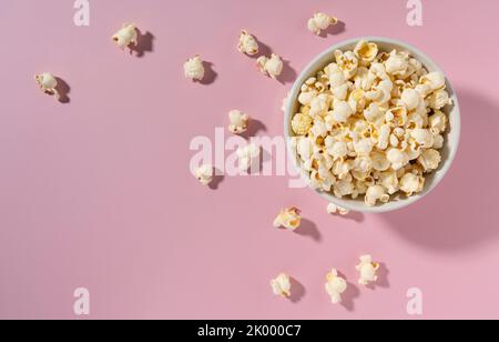 Popcorn in a white bowl placed on a pink background. View from above. Stock Photo