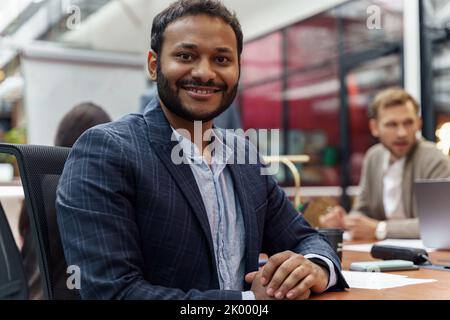 Smiling indian businessman sitting on meeting in modern office and looking at camera Stock Photo