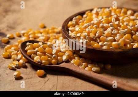 Dried corn kernels and wooden spoon in wooden bowl placed on wooden background. Corn for popcorn. Stock Photo