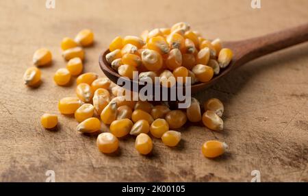 Dried corn kernels and wooden spoon placed on wooden background. Corn for popcorn. Stock Photo