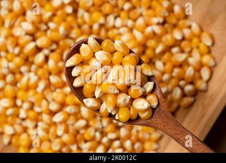 Dried corn kernels scooped with a wooden spoon. Corn for popcorn. View from above. Stock Photo