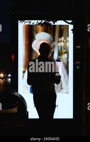 London, UK, 8th September, 2022. A man stands in front of a bus shelter advertising board close to Her Majesty the Queen's London residence, Buckingham Palace where members of the public gathered until late into the night after her death was announced during early evening. The country will now enter ten days of mourning as the monarch's 70 year reign comes to an end. Credit: Eleventh Hour Photography/Alamy Live News Stock Photo