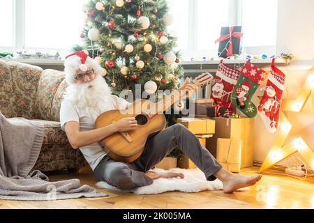 Bearded man in Santa costume with broken guitar. Musical instrument. Rock guitarist. New year. Christmas time Stock Photo