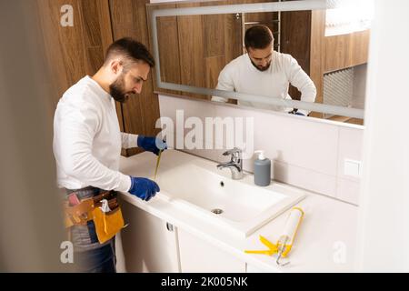 a worker installs a wash basin in a bathroom. Stock Photo