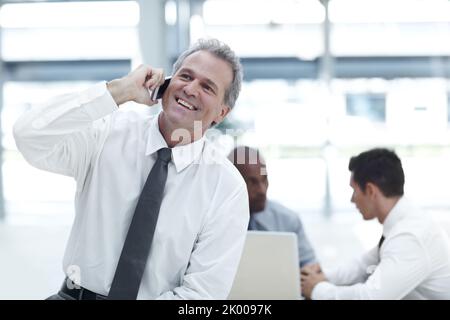 Ill see you after work. A mature businessman talking on his cellphone in front of two younger colleagues. Stock Photo