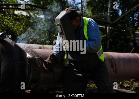 Shallow depth of field (selective focus) details with a professional welder welding an industrial metallic pipeline. Stock Photo