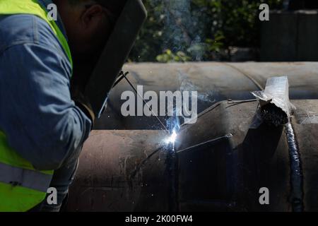 Shallow depth of field (selective focus) details with a professional welder welding an industrial metallic pipeline. Stock Photo