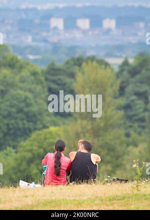 Rear/back view of man and woman sitting isolated together on rural UK hillside looking at the view of Birmingham city in the distance. Stock Photo