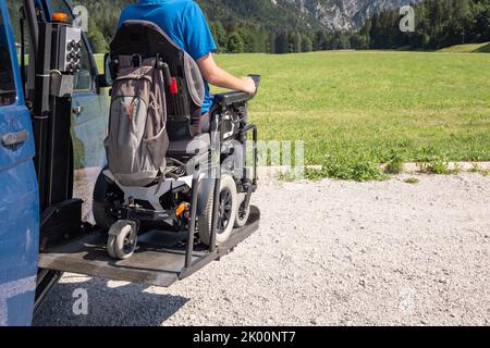 Young Caucasian man in a wheelchair using the vertical platform lift to get in the van parked in the nature Stock Photo