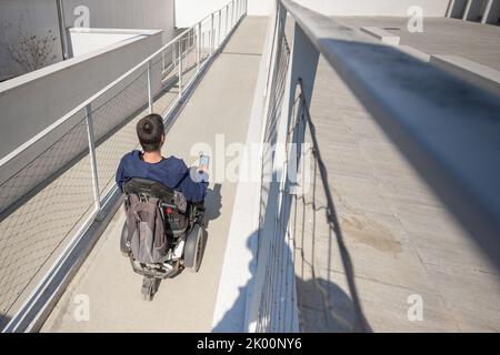 Man in a wheelchair use an accessible ramp. Stock Photo