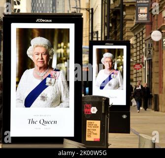 Manchester, UK, 9th September, 2022.  People walk past electronic billboards featuring Her Majesty, Queen Elizabeth II, in Manchester, United Kingdom. Her Majesty, The Queen, died, aged 96, on 8th September, 2022. Manchester City Council has said on its website that the city of Manchester will be observing the official 10-day mourning period and that: 'Residents may wish to lay flowers to mark Her Majesty’s death. You can lay flowers at St Ann's Square'. Credit: Terry Waller/Alamy Live News Stock Photo
