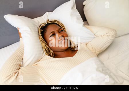 african american woman trying to sleep but the noise bothers her she is covering the ears with a pillow Stock Photo