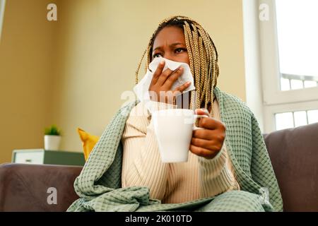 afro american woman covered with blanket blowing running nose holding tea cup Stock Photo