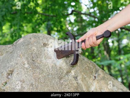 hand of the knight who tries to extract the Excalibur Sword stuck in the rock in the enchanted forest Stock Photo