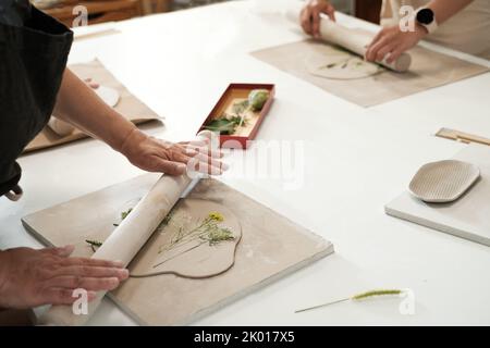 Pottery workshop in studio. Hands working with clay on the table. Adult learning to do ceramic plates. Pottery as hobby and leisure activity. Close-up Stock Photo
