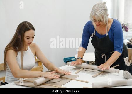 Pottery workshop in creative studio. Woman working with clay on the table. Adults learning to do ceramic plates. Pottery as hobby and leisure activity Stock Photo