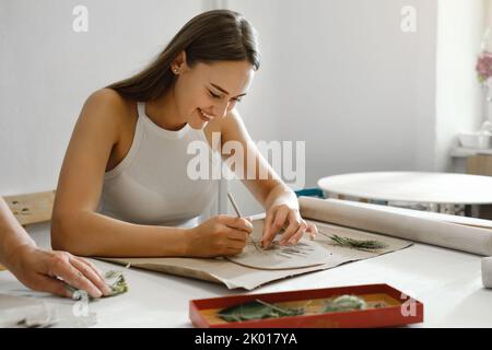 Pottery workshop in studio. Young woman working with clay on the table. Adult female learning to do ceramic plates. Pottery as hobby and leisure Stock Photo