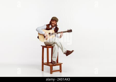 Portrait of stylish man playing guitar, performing isolated over white studio background. Smiling. Cheerful song Stock Photo