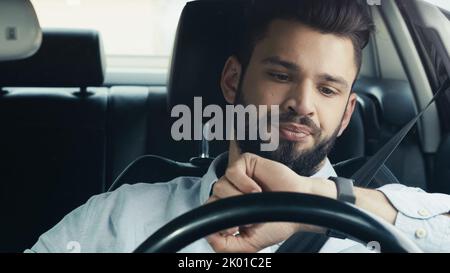 displeased bearded man driving car and looking at wristwatch,stock image Stock Photo