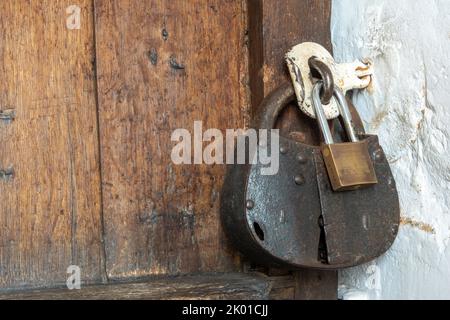 A very large iron antique padlock and a small modern brass padlock locking a hasp on an ancient church timber door Stock Photo