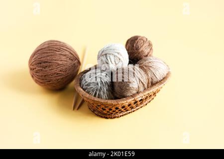 Gray and brown balls of knitting threads on a yellow background in a basket with knitting needles Stock Photo