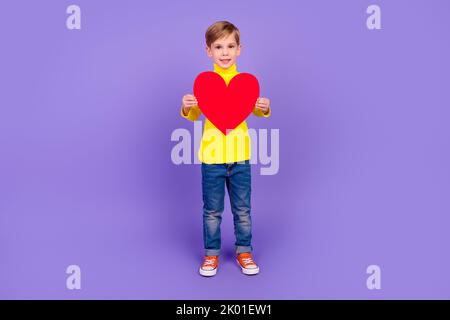 Full length photo of pretty funny small son wear yellow turtleneck holding large red heart isolated violet color background Stock Photo