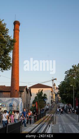 Group of people walking through the entrance of the Viseu fair, with a steam factory column and a tram track that goes up to the top of a hill. Stock Photo