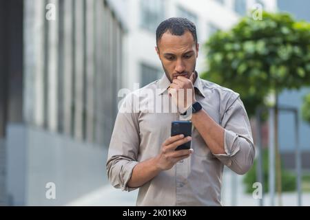 Thinking and sad muslim businessman reading message from smartphone, man outside office building using phone depressed reading bad news Stock Photo