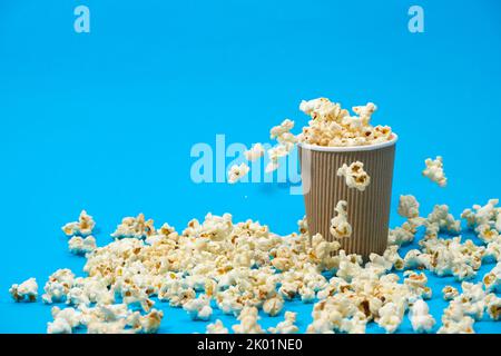 Popcorn is poured into a paper brown glass on a blue background with place for text. Stock Photo