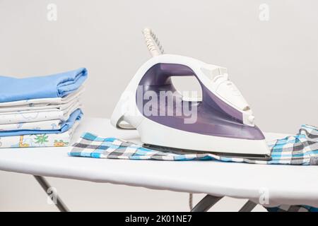 Iron on the ironing board and plaid children's shirt on a white background. Care of children's clothing Stock Photo