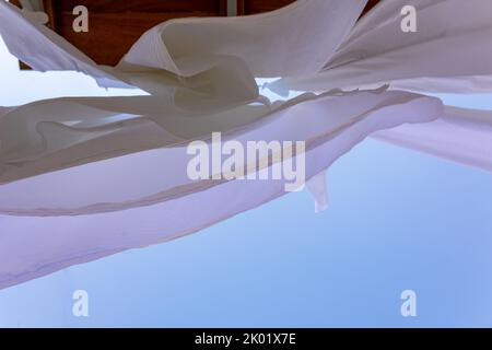 White linen drying on clothesline in fishing village of Symi, Island in Greece. Snow-white sheets scatter in wind. Bottom view. High quality photo Stock Photo