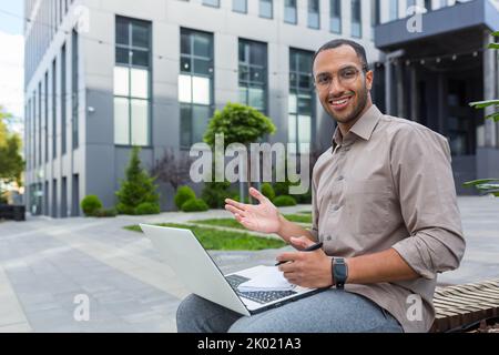 Portrait of young happy African American man, student outside campus smiling and looking at camera, teacher using laptop for online learning and video calling with students Stock Photo