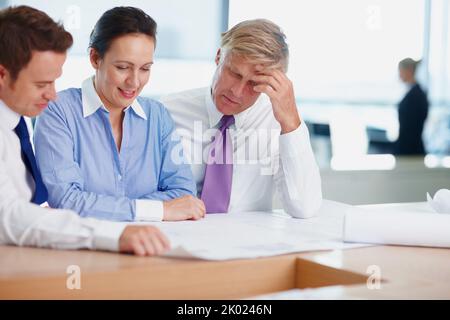Architects discussing on blueprint. Three architects sitting at table and looking at a project. Stock Photo